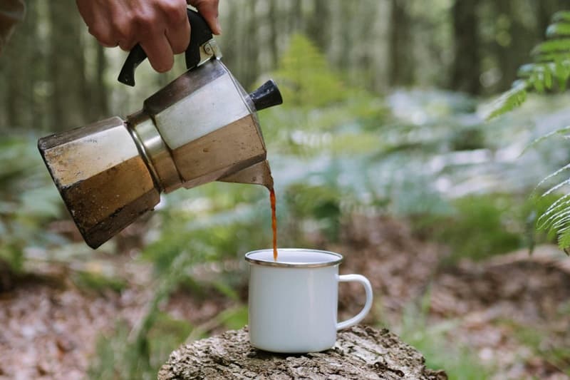 quelqu'un verse du café dans une tasse de seconde main dans un décors nature, durant une pause café écoresponsable.