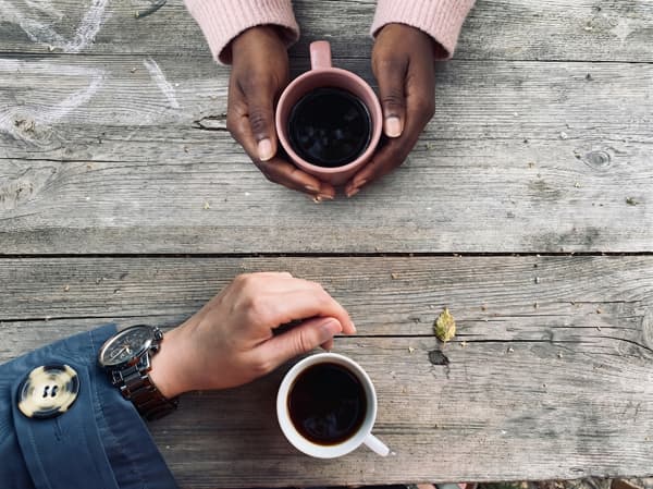 Les mains de 2 collègues qui boivent un café dans une tasse de récup' durant une pause café éco-responsable.